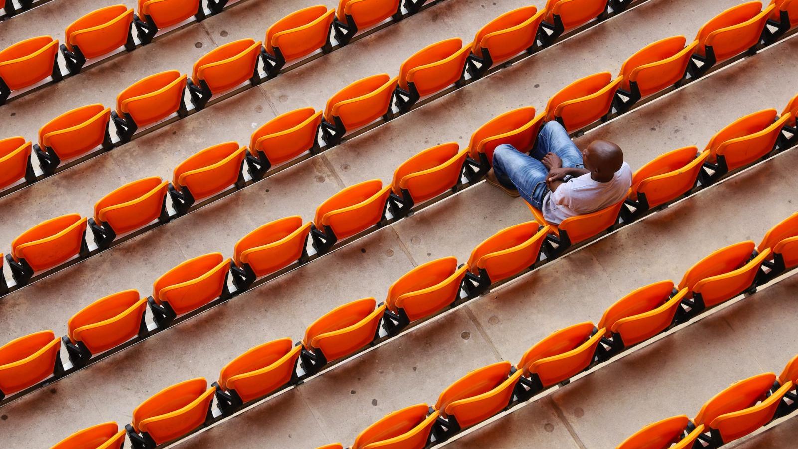 A person sitting in a row of orange football stadium seats.